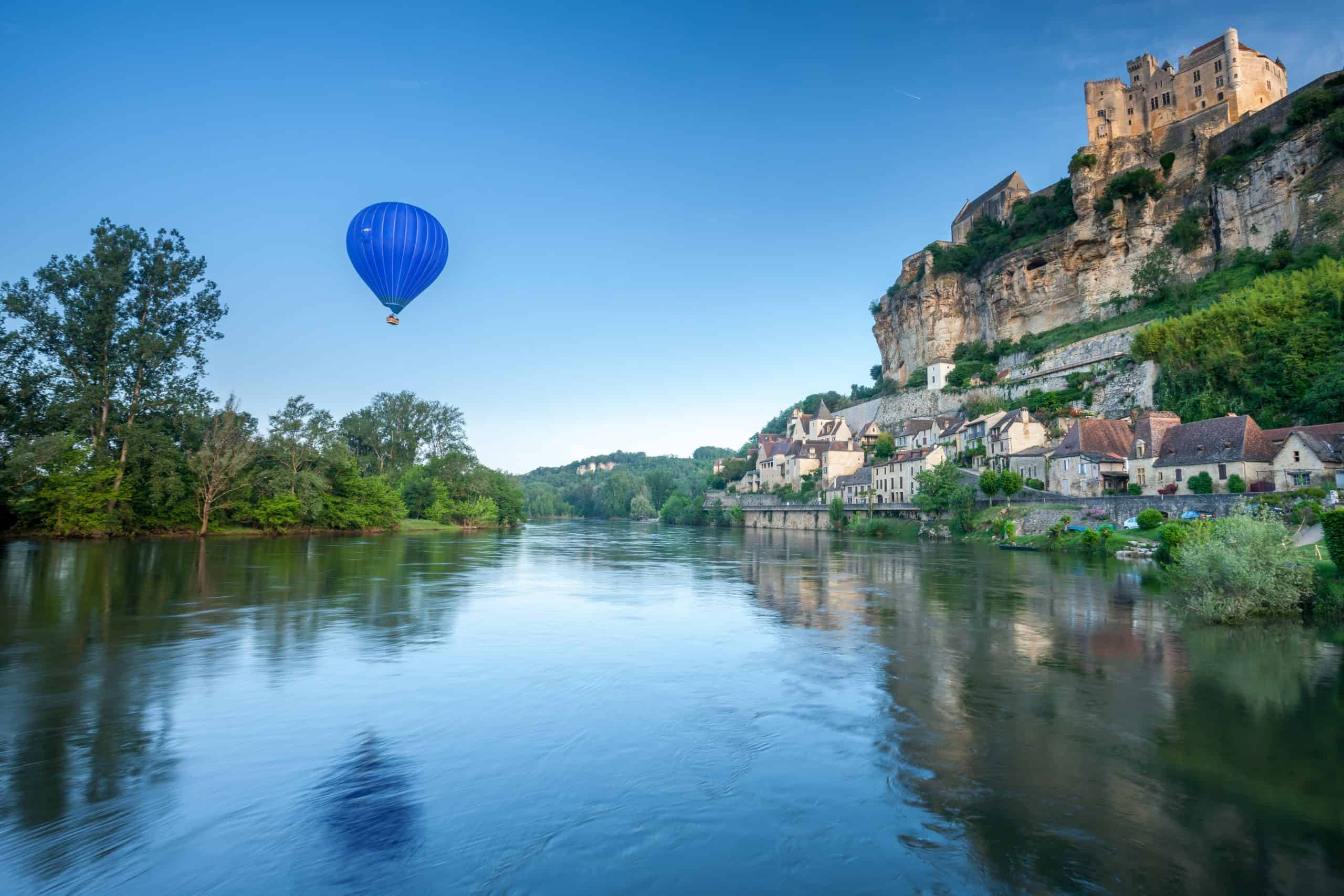 Hot air balloon over the Périgord river and historic castle.