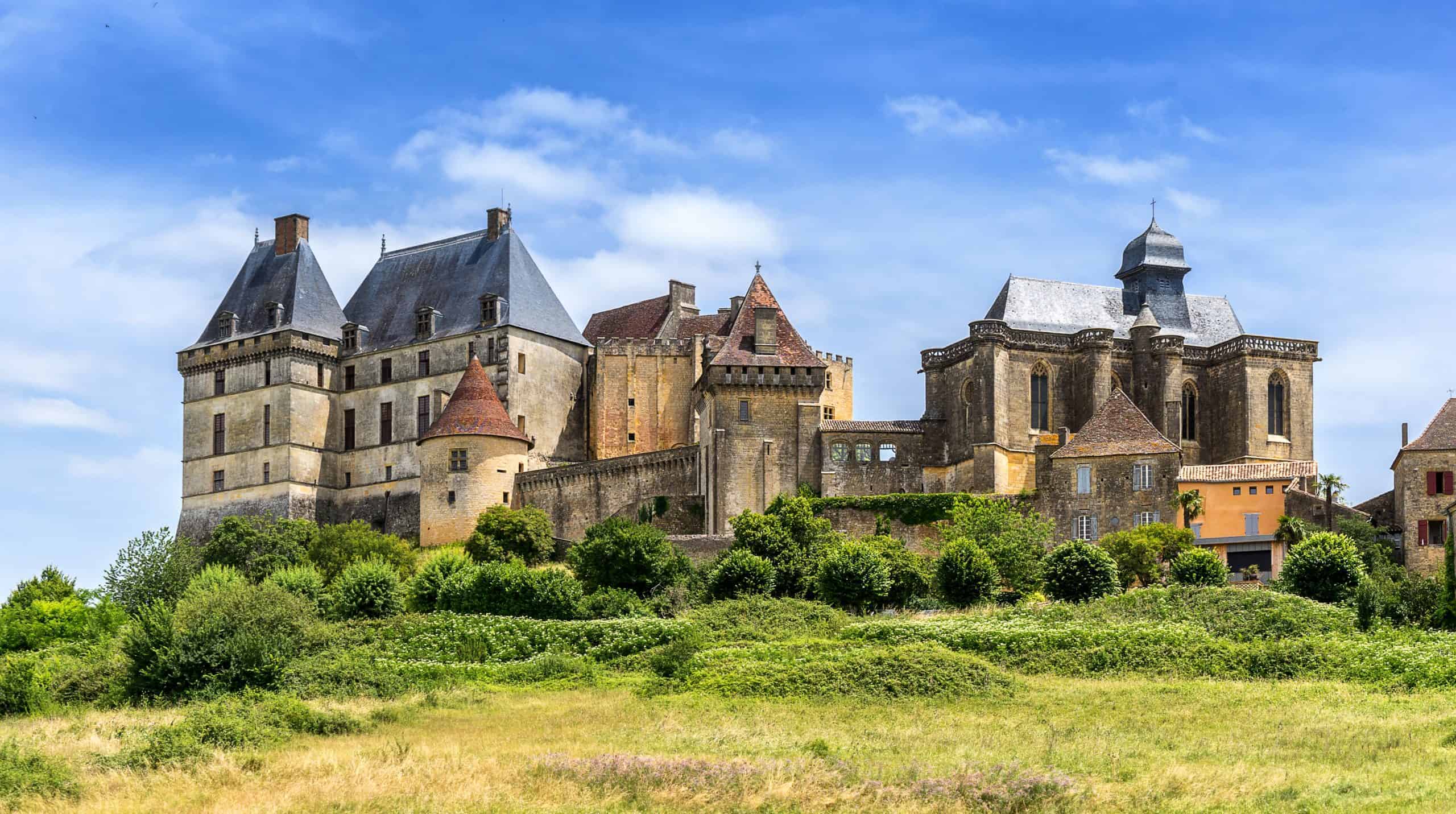 Historic castle in Périgord with towers and stone walls, scenic landscape.
