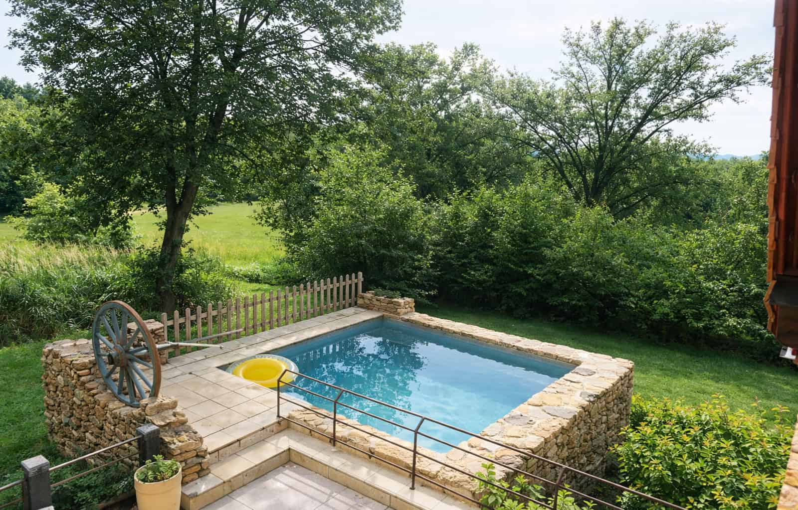 Outdoor swimming pool with stone border, surrounded by trees and nature for relaxation and leisure.