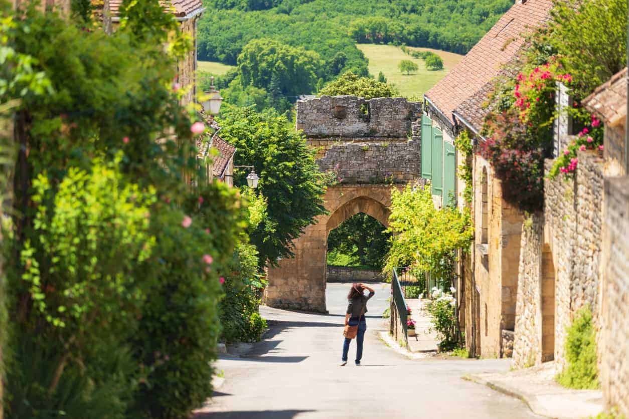 Scenic view of a Périgord village street with historic stone buildings and lush greenery.