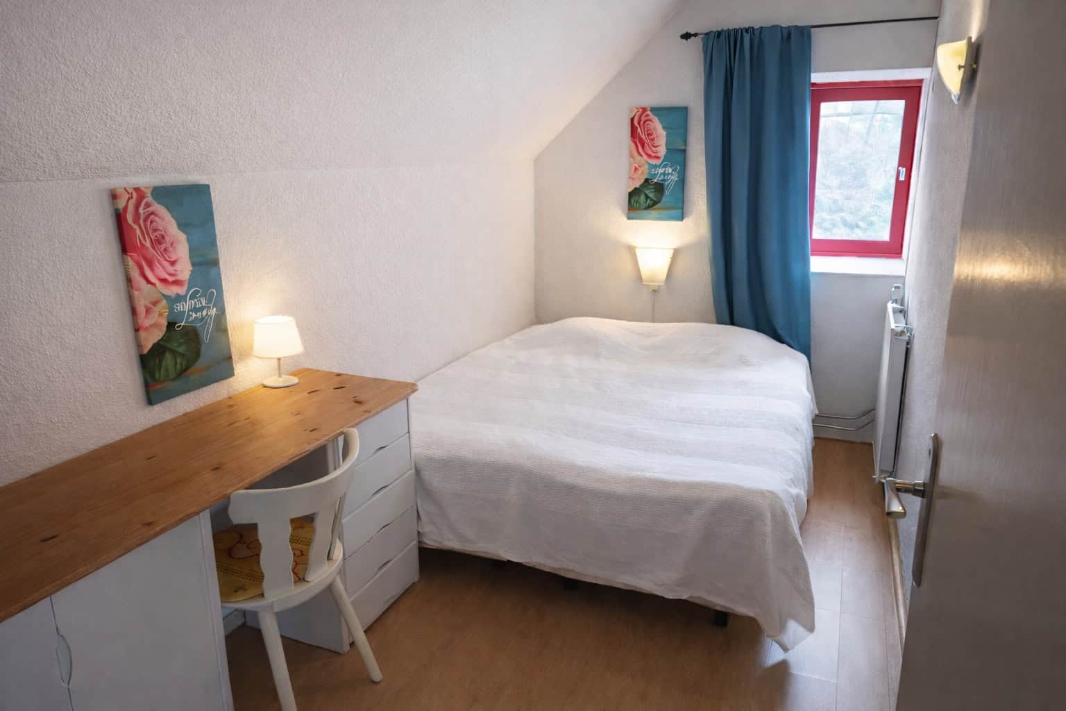 Cozy bedroom with white bedding, vibrant floral art, and natural light from a window with blue curta.