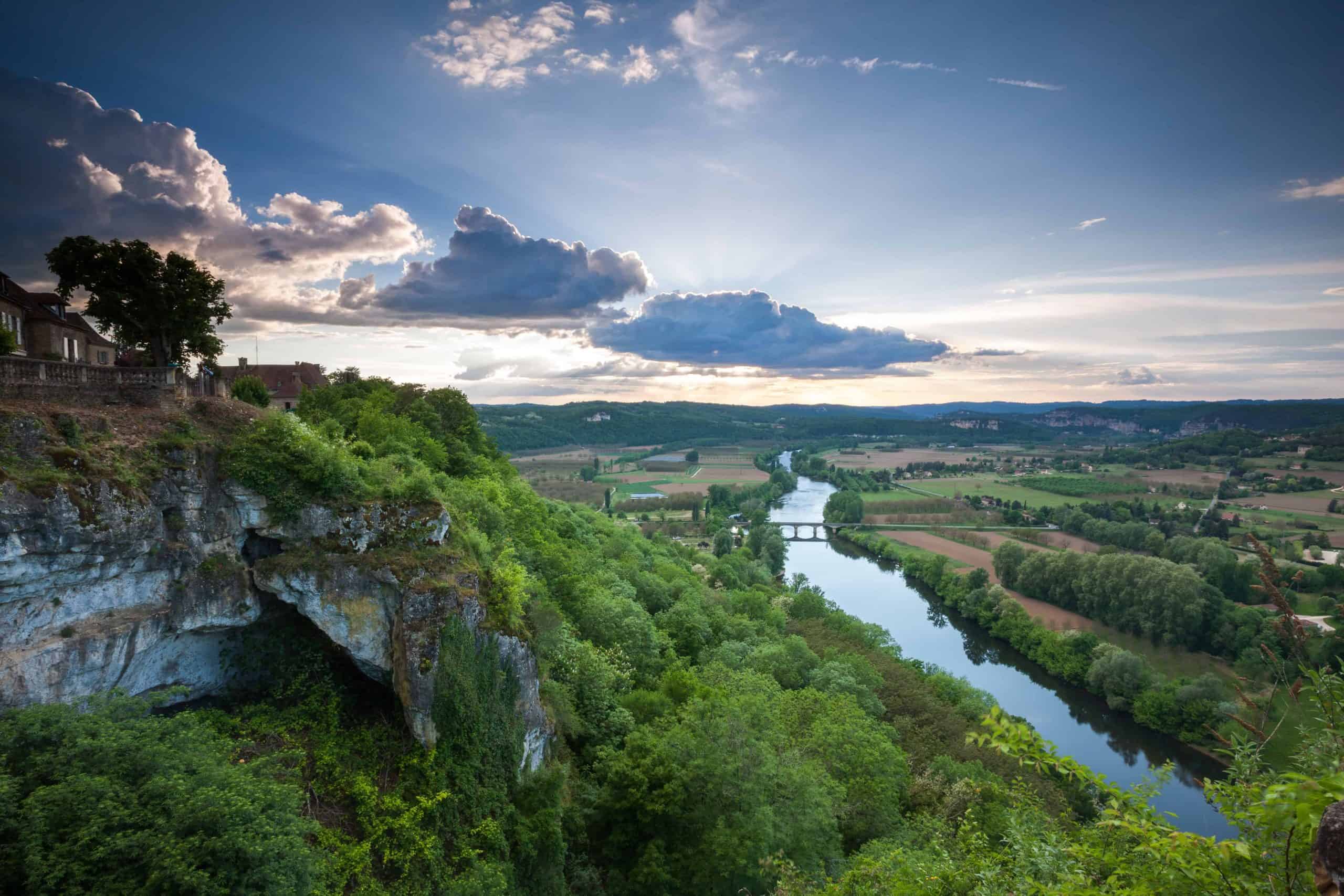 Beautiful river valley with cliffs, lush greenery, and a flowing river under a partly cloudy sky.