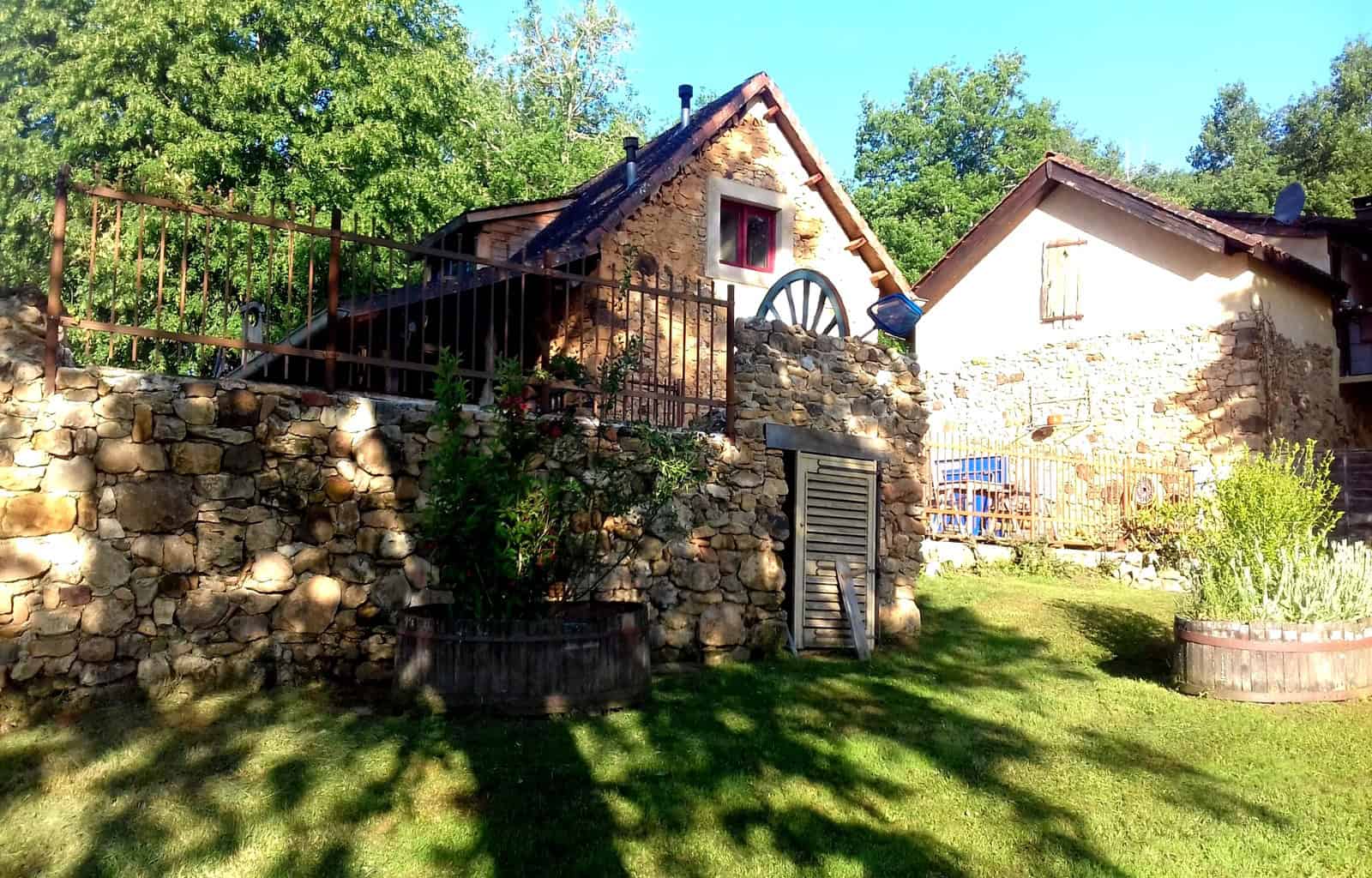 Rustic stone house with a sloped roof, surrounded by lush greenery and a well-maintained garden.
