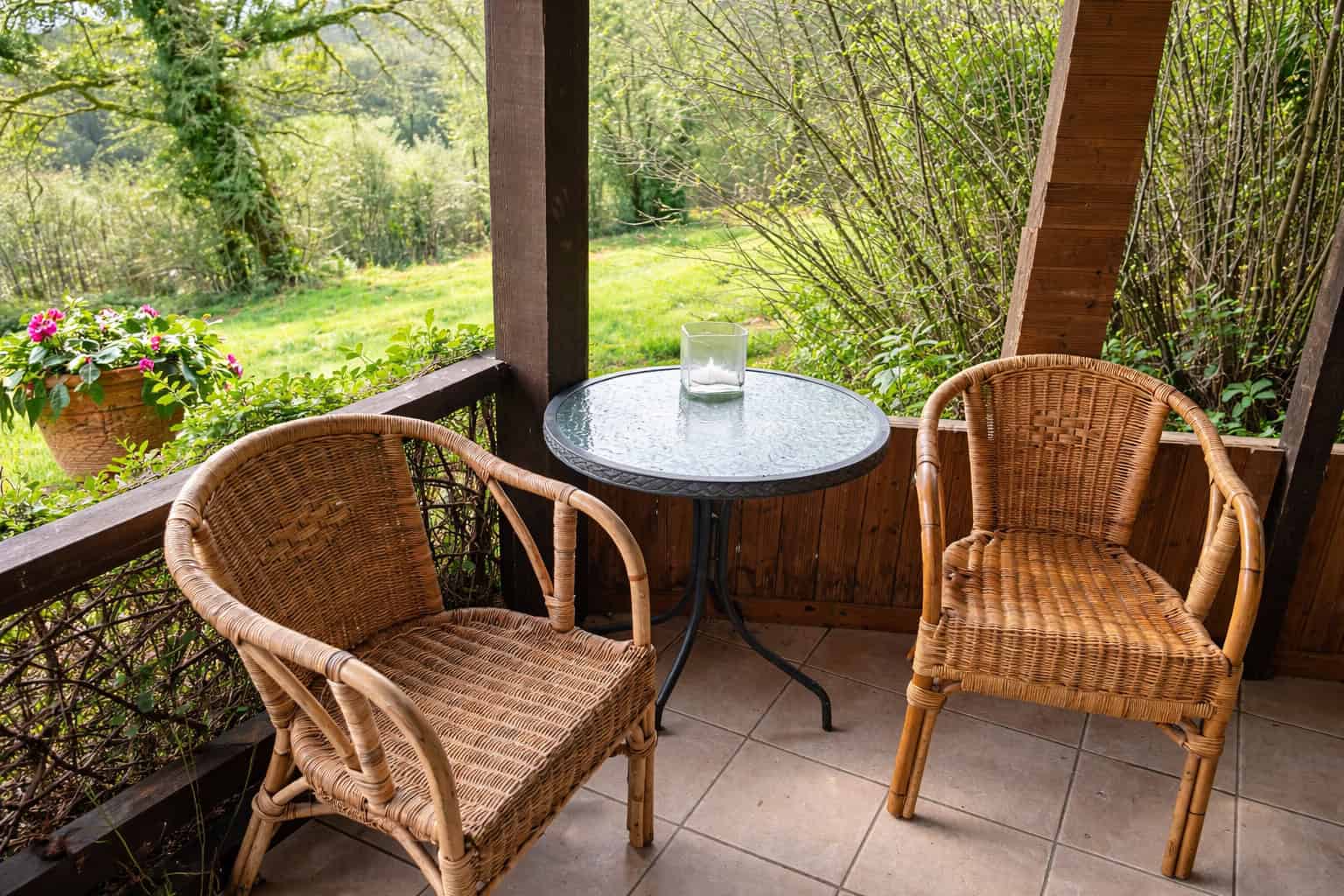 Balcony with two rattan chairs and a small round table overlooking lush garden scenery. Perfect for.